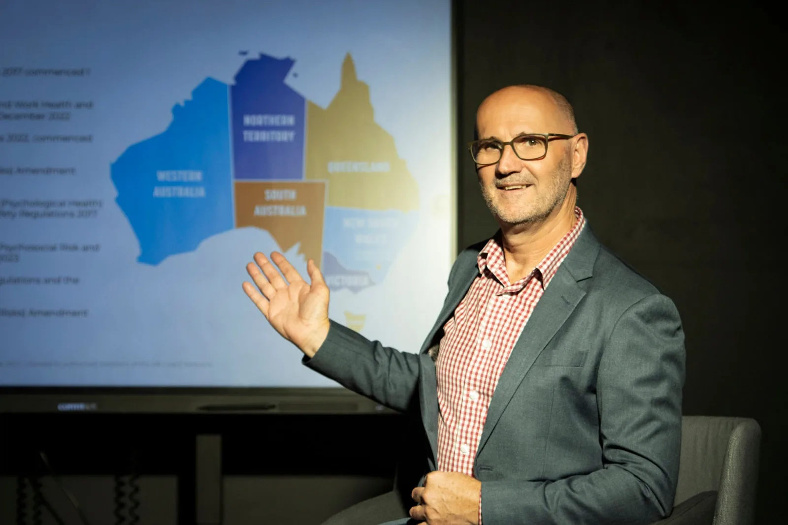 Rod Smith presenting, gesturing to a map of Australia on the screen behind him